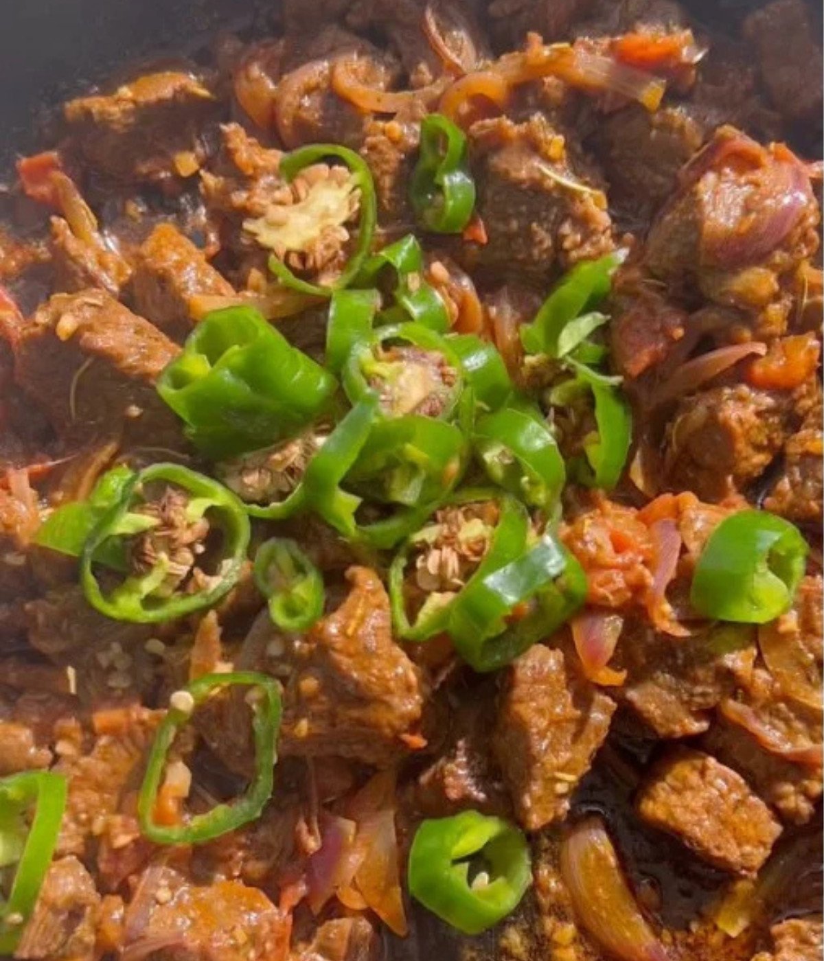 Chopped beef cooking in a black pan with jalapenos.