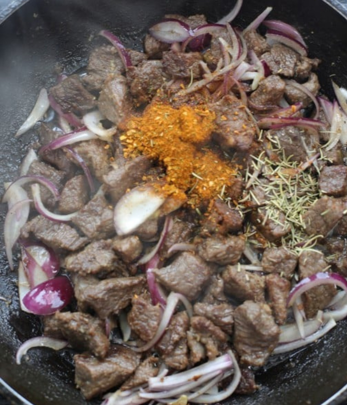 Chopped beef cooking in a black pan with red onions, berbere and rosemary.