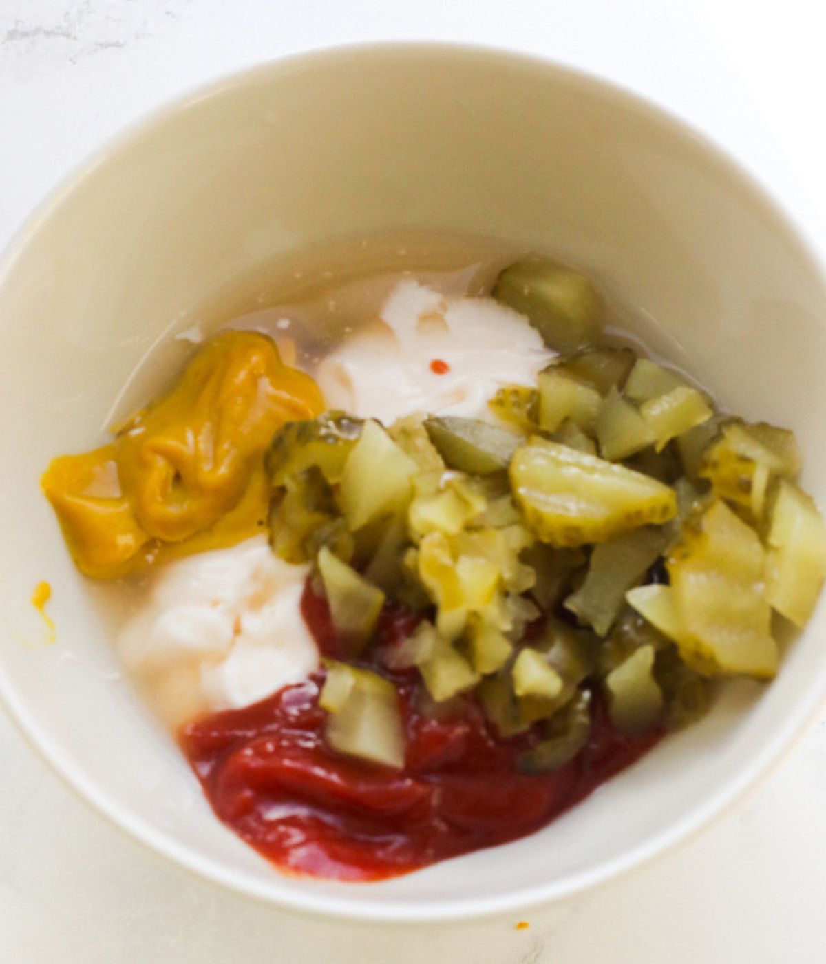 Mustard, ketchup, mayonnaise and gherkins in a bowl.