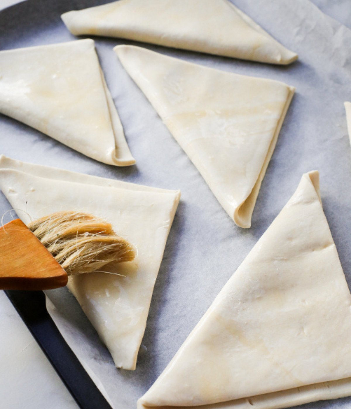 Square puff pastry sheets folded into a triangle on a lined baking tray basted with egg wash.