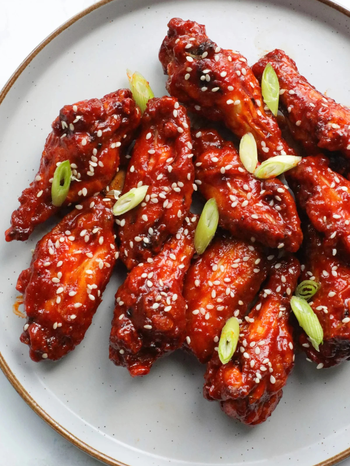 Korean wings on a grey plate topped with sesame seeds and scallions.