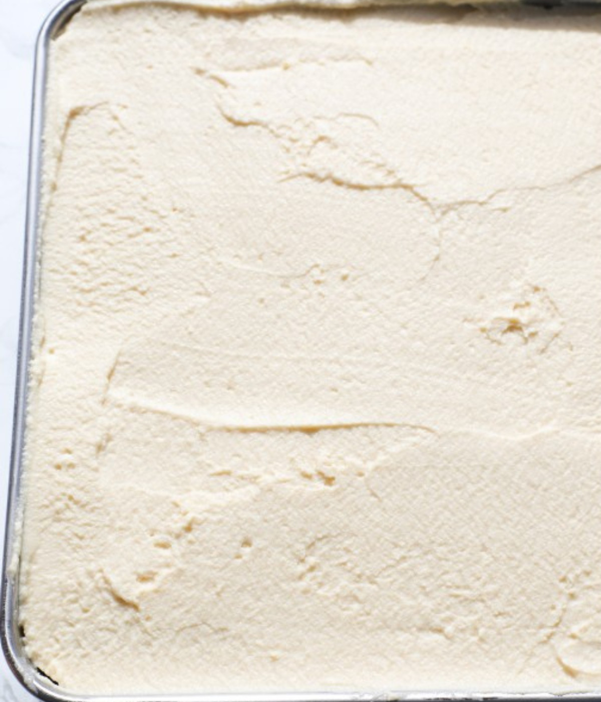Lady fingers laid in a square silver baking tin with a layer of biscoff cream smoothed on top.