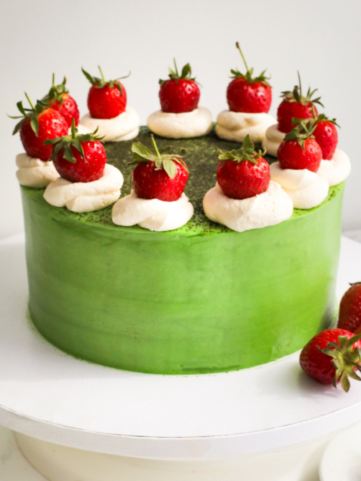 Matcha strawberries and cream cake on a white board.