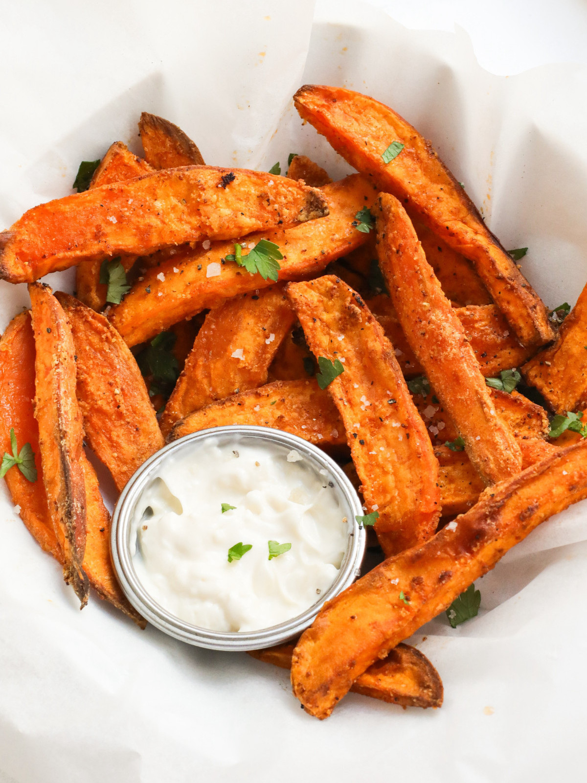 Crispy air fried sweet potatoes in a plate with garlic sauce in a silver pot.