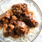 Jamaican oxtail on top of white rice in a plate.
