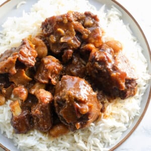 Jamaican oxtail on top of white rice in a plate.