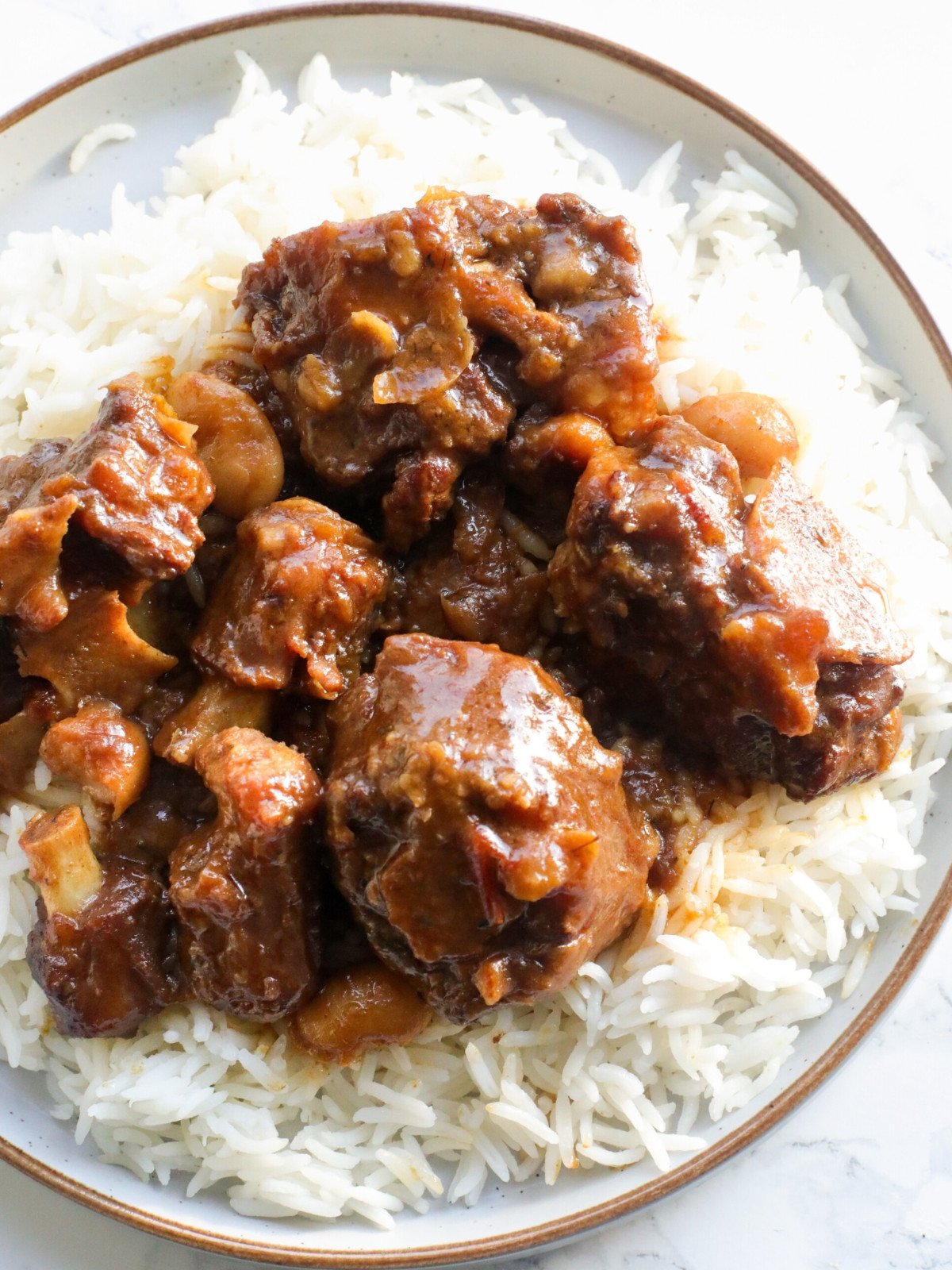 Jamaican oxtail served ob rop of white rice in a plate.
