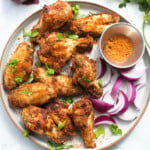 Nigerian style suya spice wings on a plate with red onions and herbs.