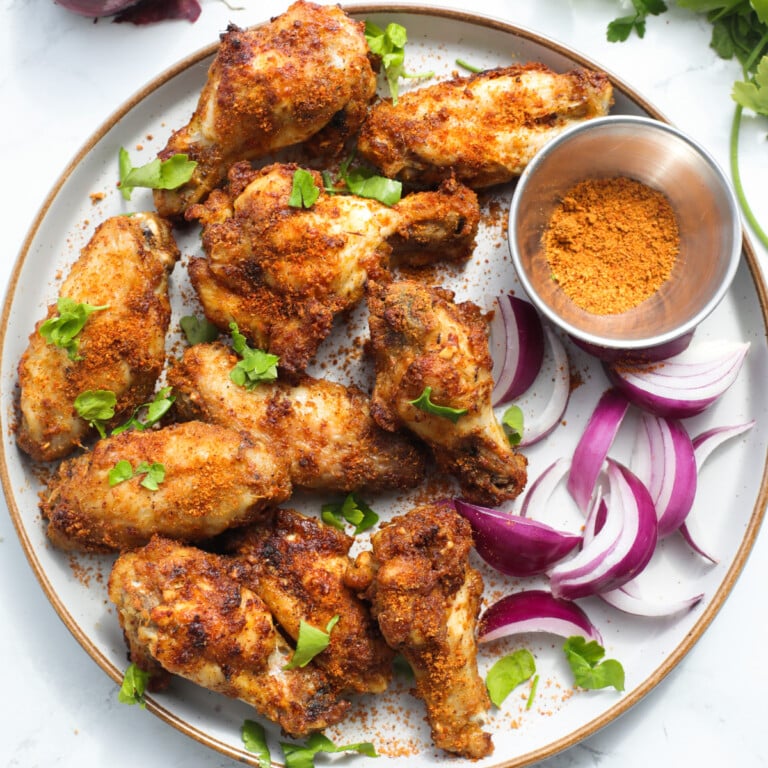 Nigerian style suya spice wings on a plate with red onions and herbs.