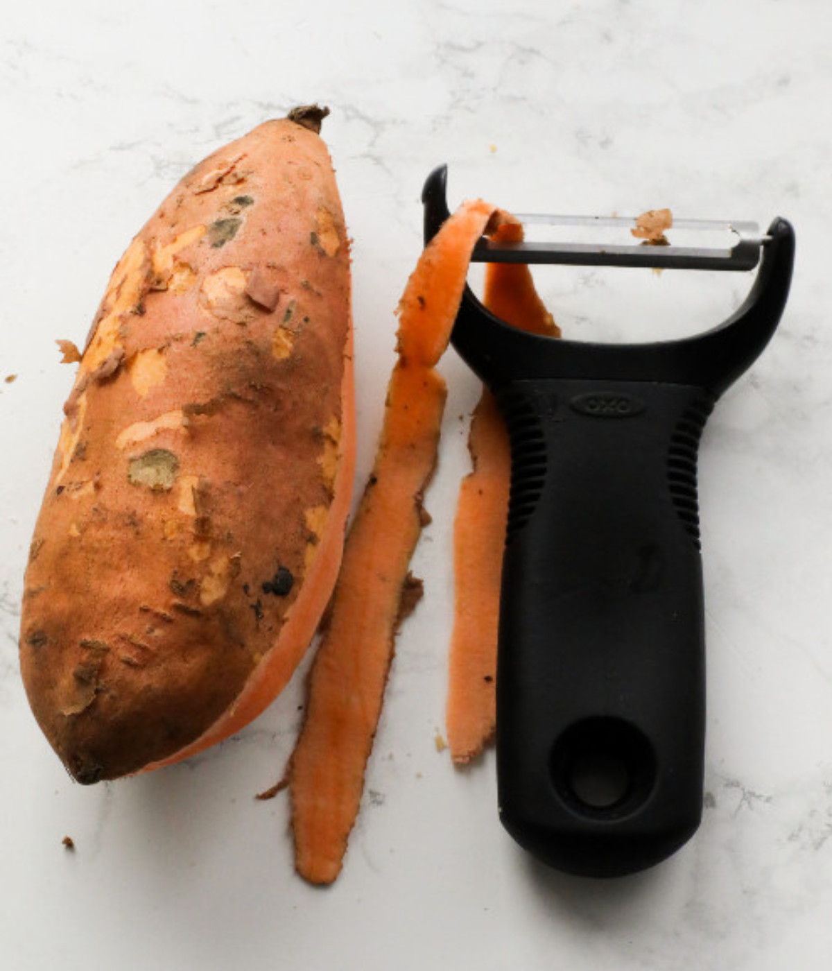 Peeled sweet potato on a table with a black potato peeler.