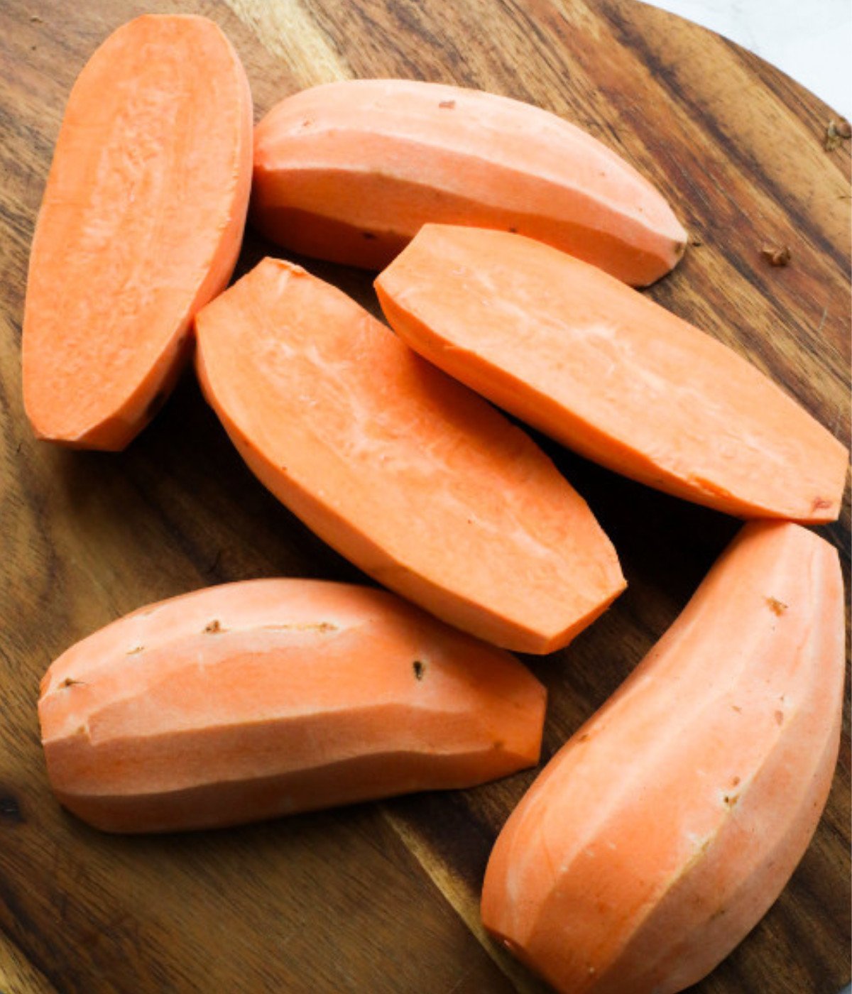 Peeled sweet potatoes on a wooden chopping board.