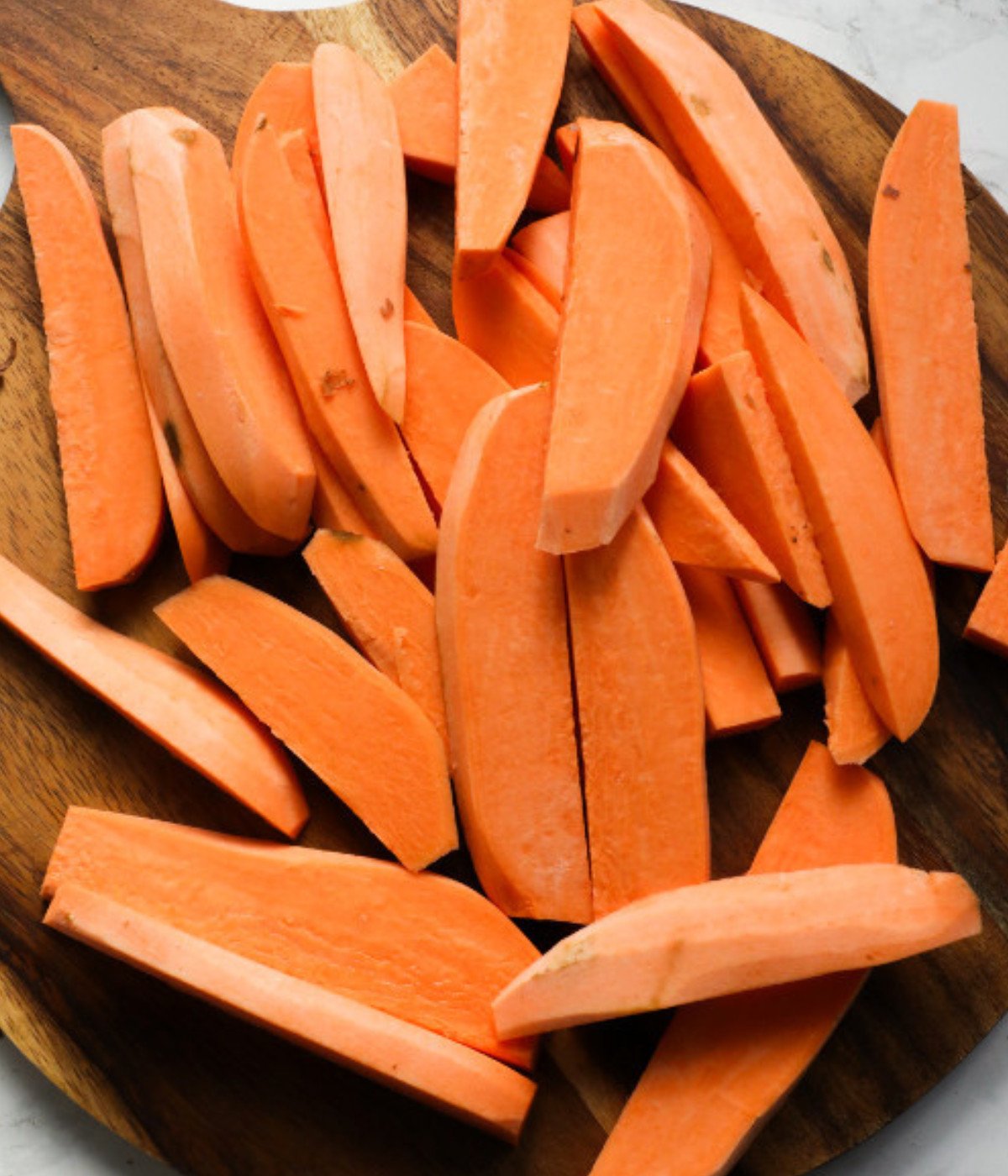 Sliced sweet potatoes on a wooden chopping board.