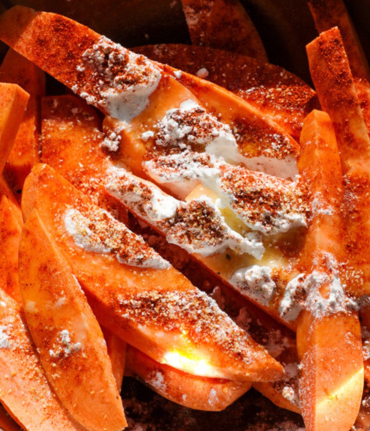 Sliced sweet potatoes seasoning, oil and baking powder in a silver bowl.