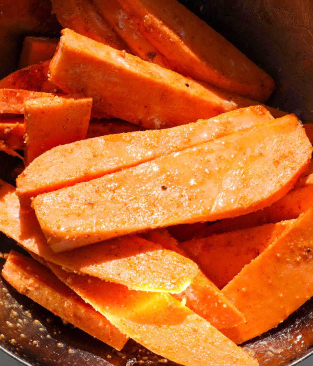 Sliced sweet potatoes seasoning, oil and baking powder mixed in a silver bowl.