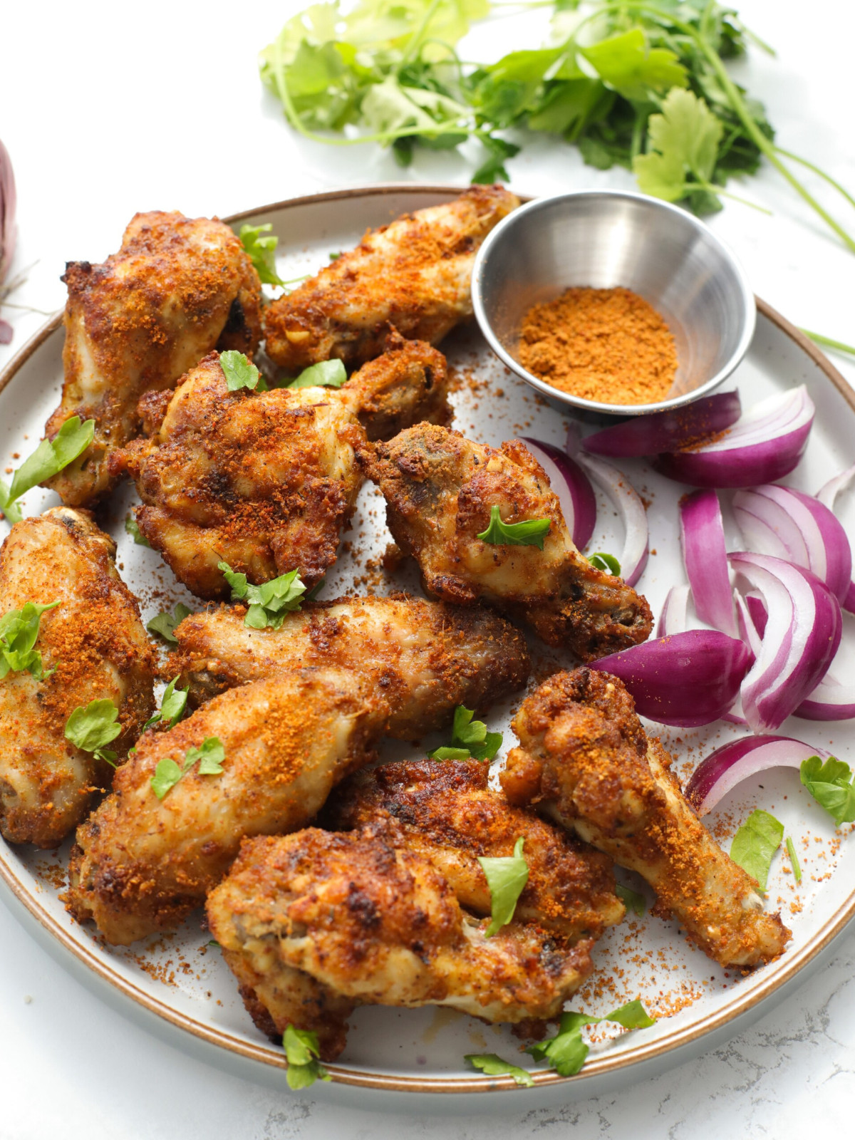 Suya wings on a plate topped with fresh herbs, red onions and suya powder.