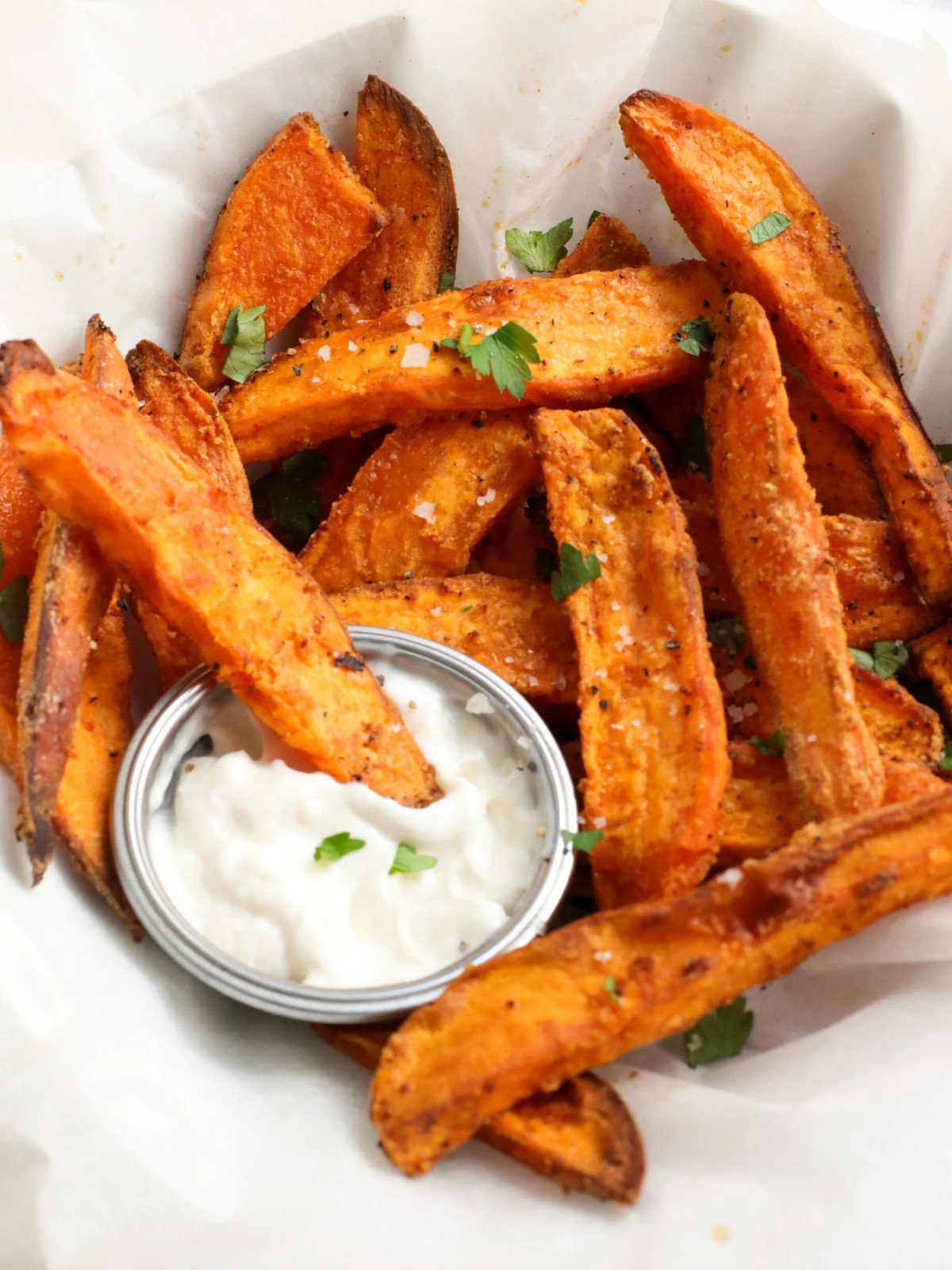 Sweet potato wedges in a plate topped with herbs and served with garlic sauce.