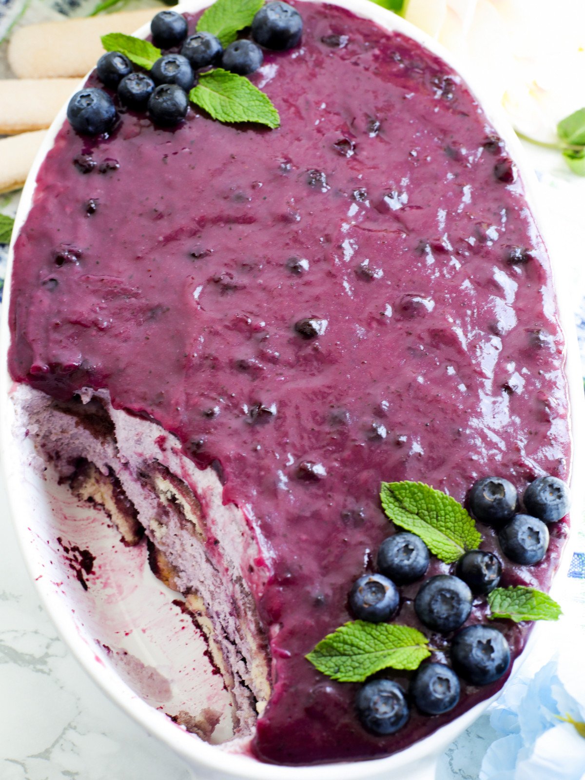 Blue berry tiramisu in a white dish with mint leaves.
