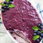Blue berry tiramisu in a white oval dish topped with blueberries and mint leaves.