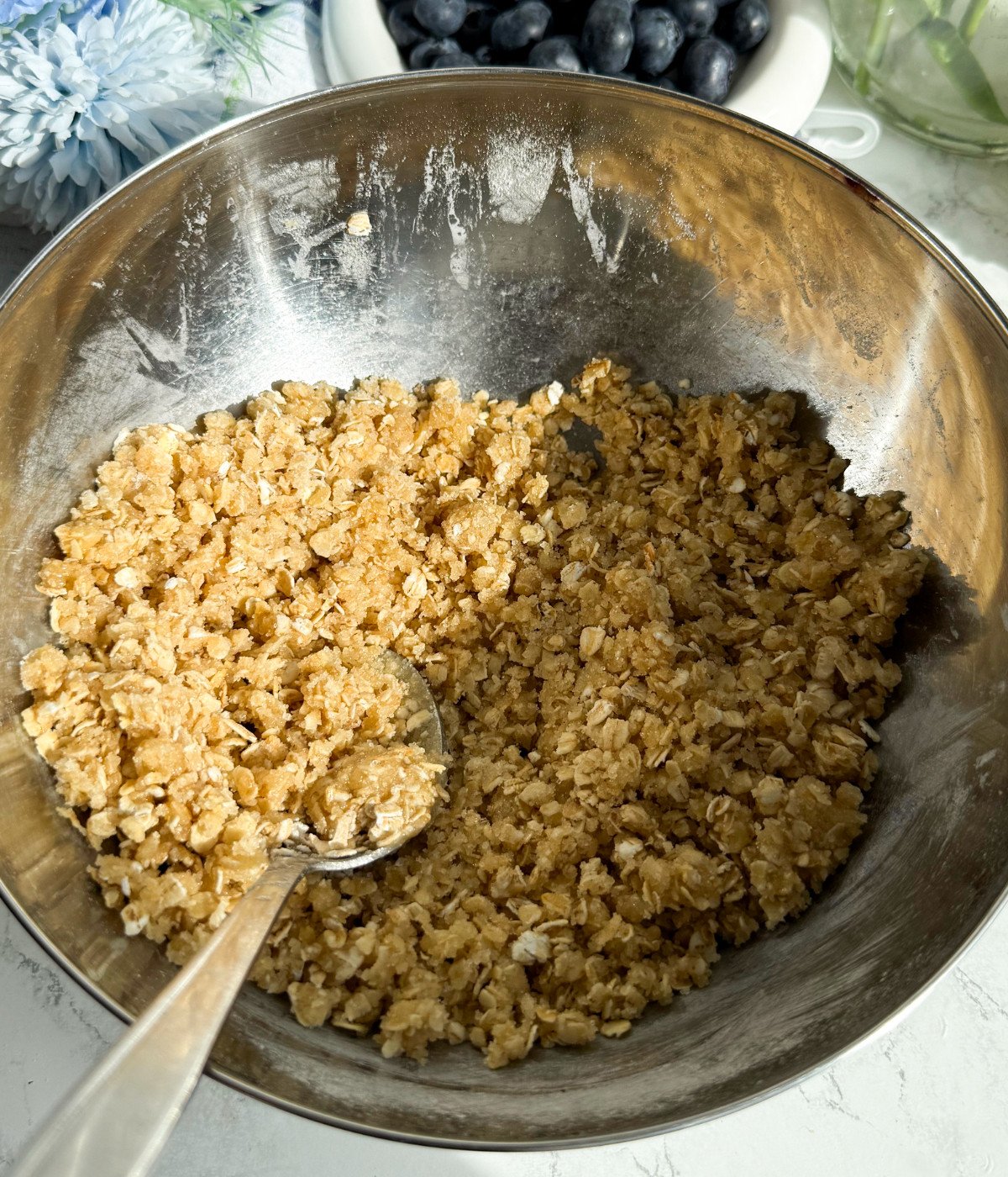 Brown sugar, flour, oats, melted butter and cinnamon mixed in a silver bowl.