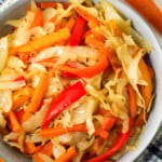 Cooked white cabbage, onions, red bell peppers, carrots and thyme in a bowl.