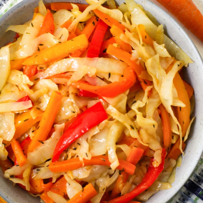Cooked white cabbage, onions, red bell peppers, carrots and thyme in a bowl.
