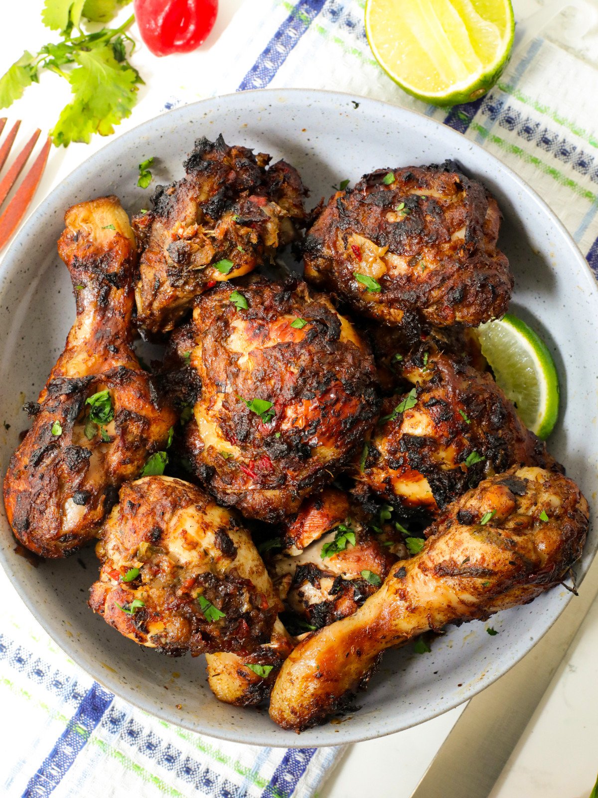 Jerk drumsticks and thighs in a blue bowl with lime and herbs.