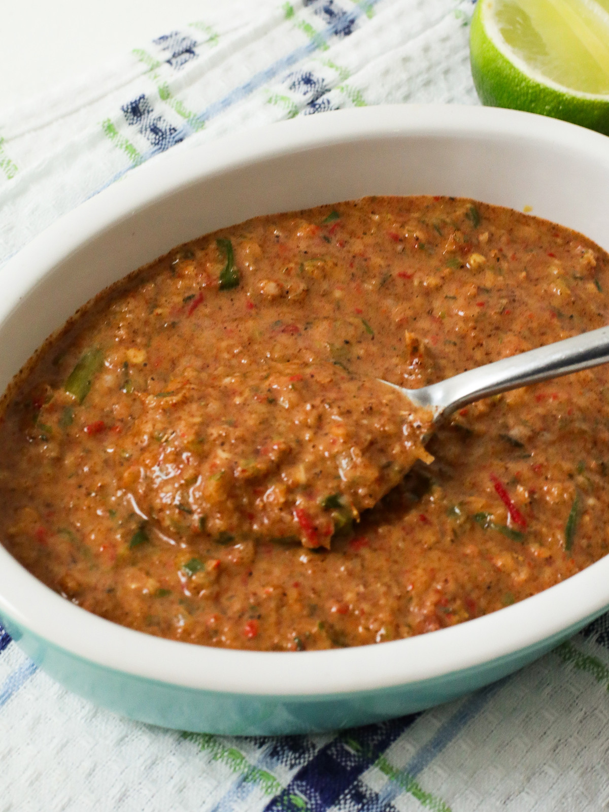 Jerk marinades in a white and blue oval bowl with a silver spoon.