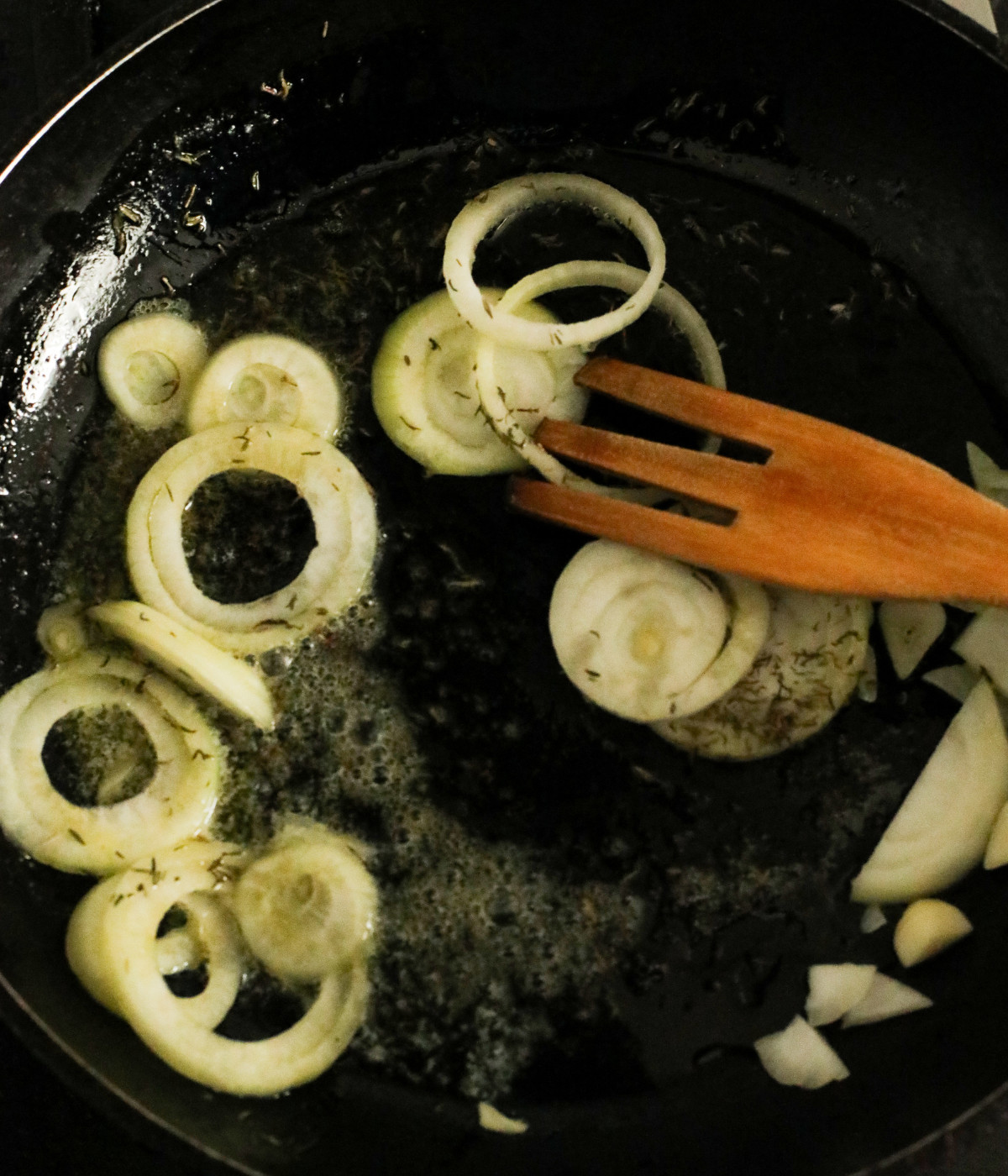 Oil, butter, onions, garlic, and thyme cooked in a black pan.