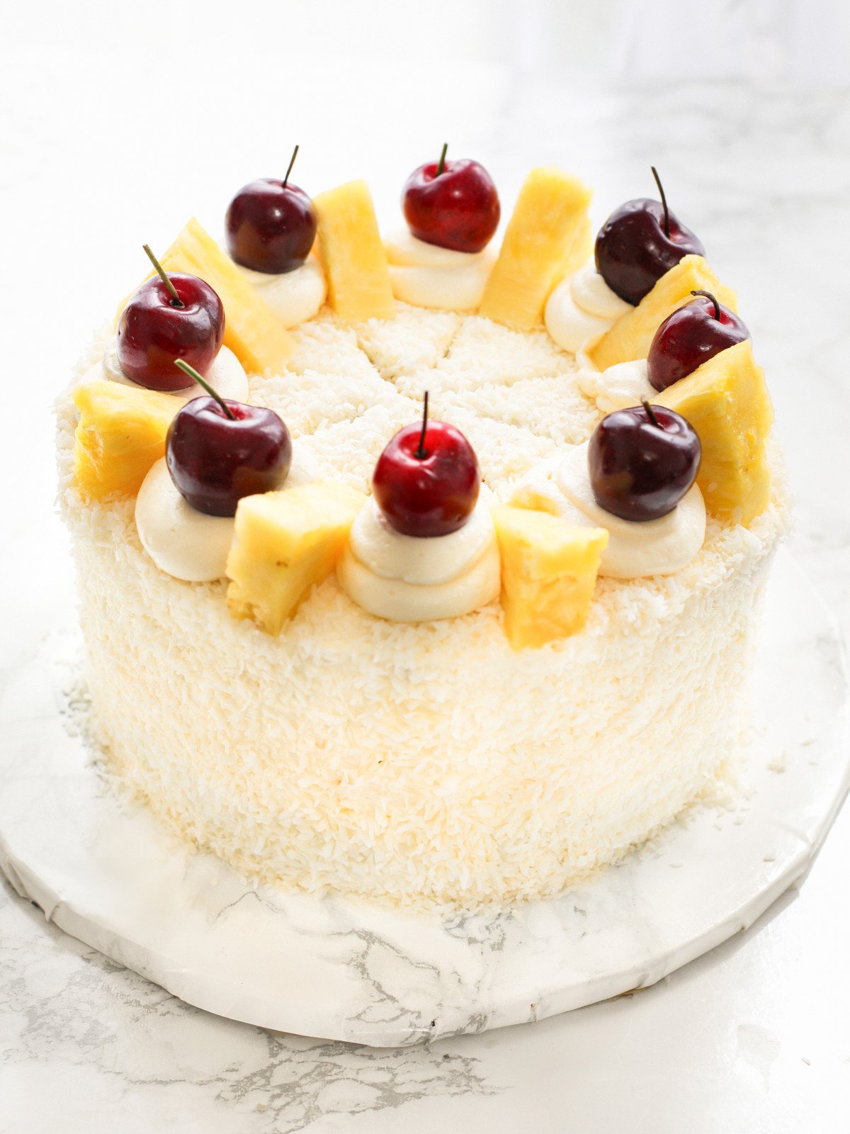 Pina coladas cake topped with pineapple, cherries and coconut flakes.