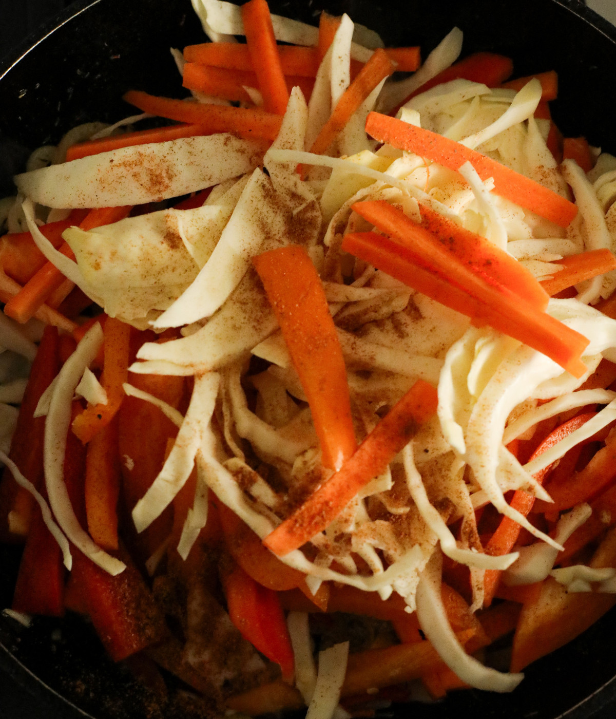 Sliced cabbage, carrots, red bell peppers, onions and seasoning in a pan.