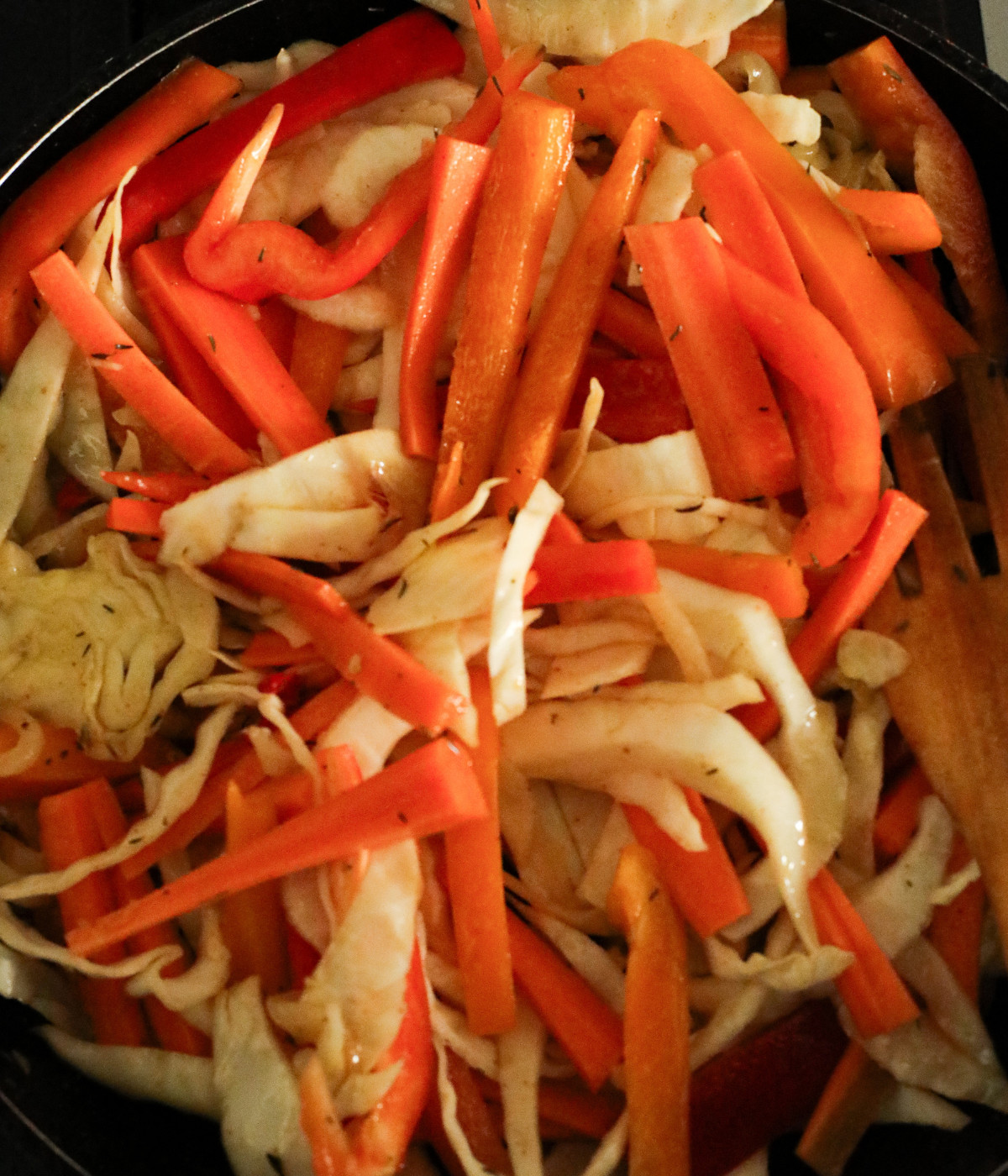 Sliced cabbage, carrots, red bell peppers, onions, water and seasoning in a pan.