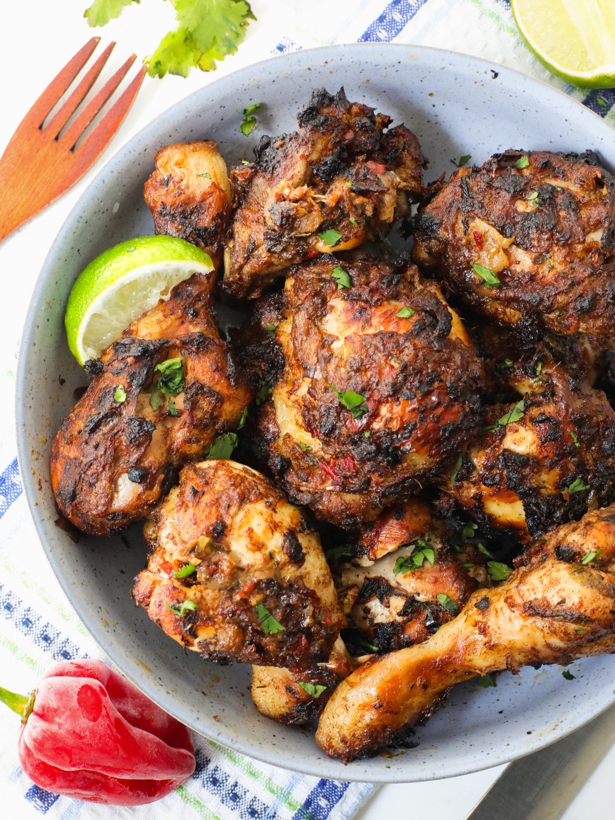 Spicy jerk drums and thighs in a blue bowl garnished with parsley and lime.
