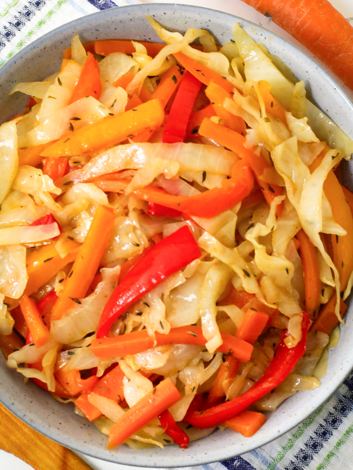 Steam carrots, red bell pepper, thyme, white cabbage in a bowl.