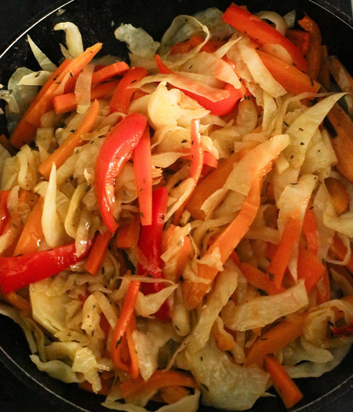 Steamed cabbages, carrots, red bell peppers in a pan.
