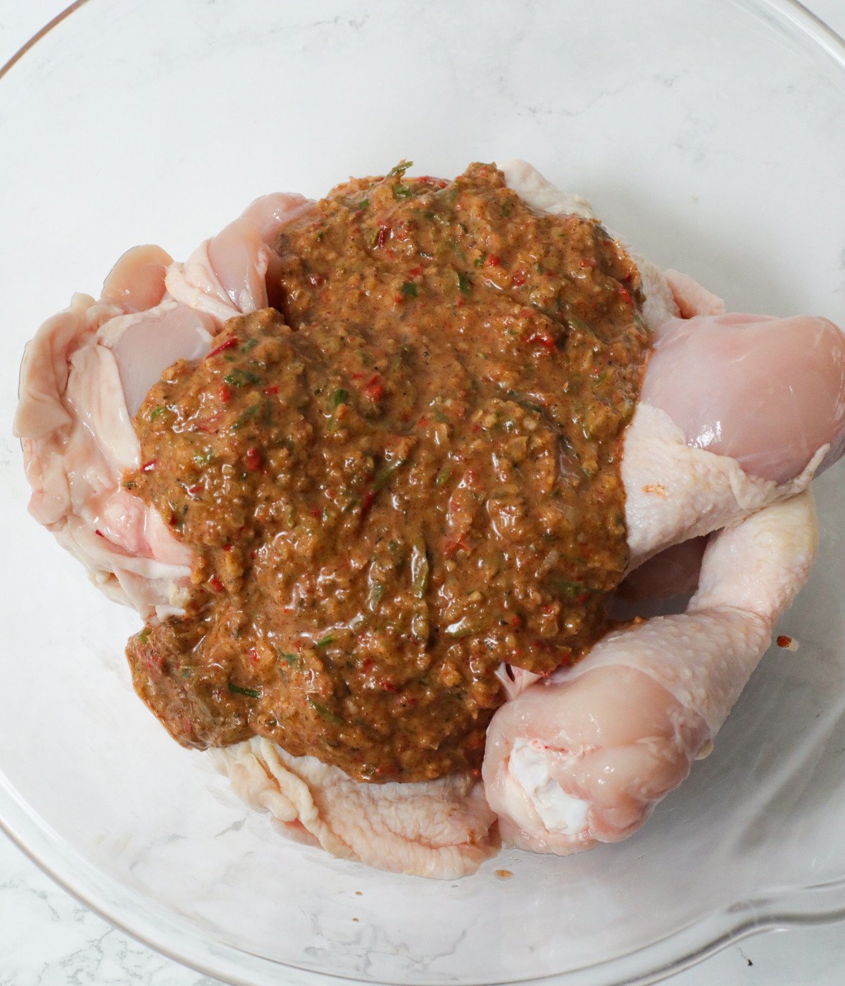Uncooked thighs, drums and jerk marinade in a glass bowl.