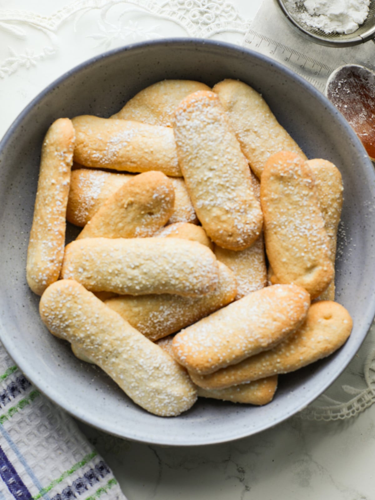 Homemade ladfinger biscuits in a blue bowl on a table.