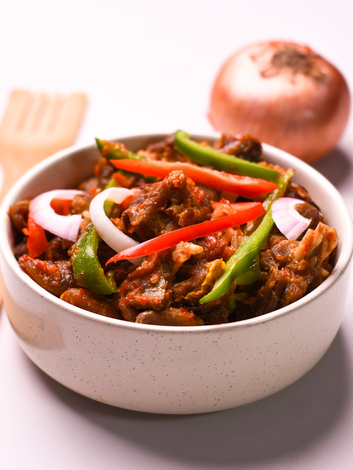 Nigerian peppered goat meat in a white bowl with peppers and onions.