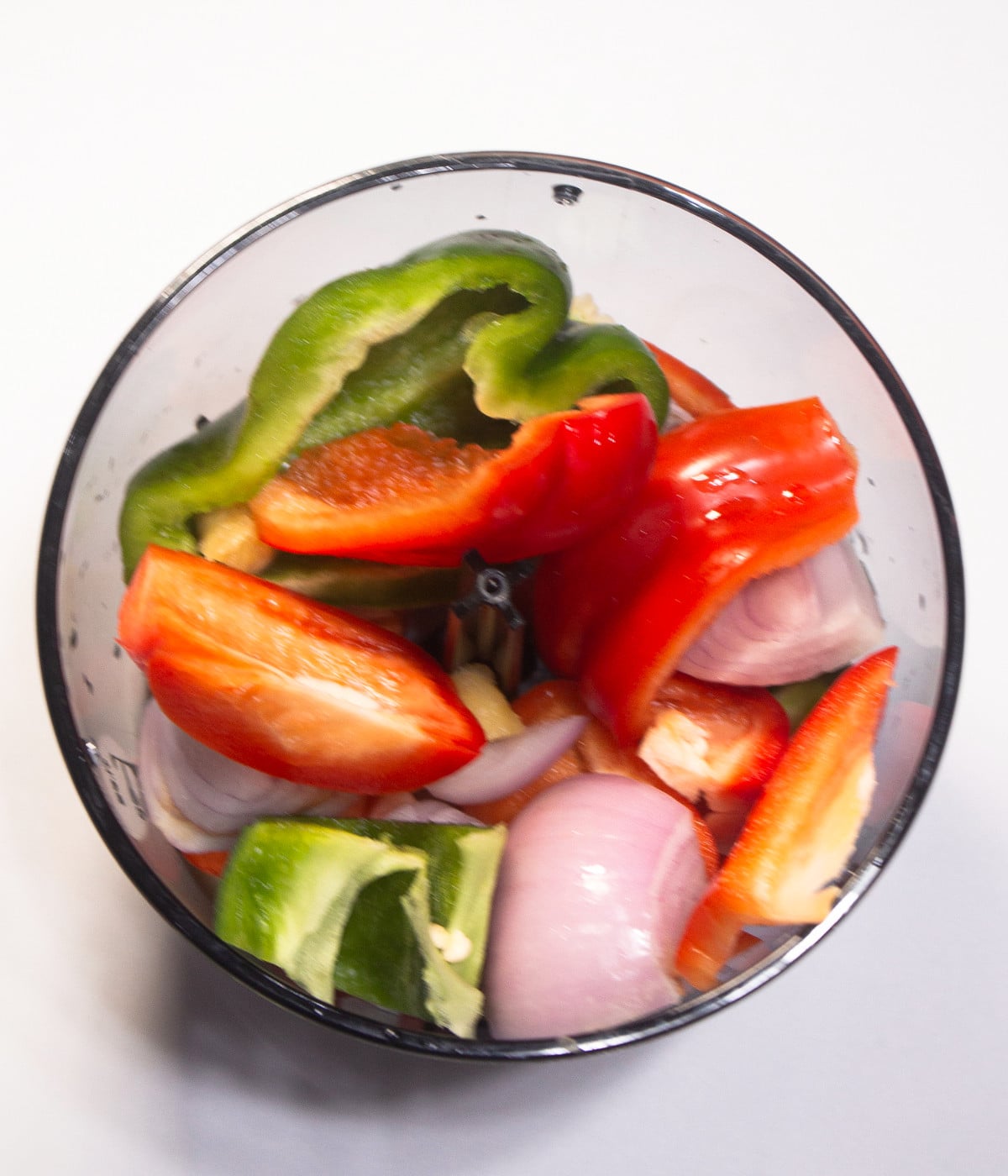 Red bell peppers, green peppers and onions in a blender.