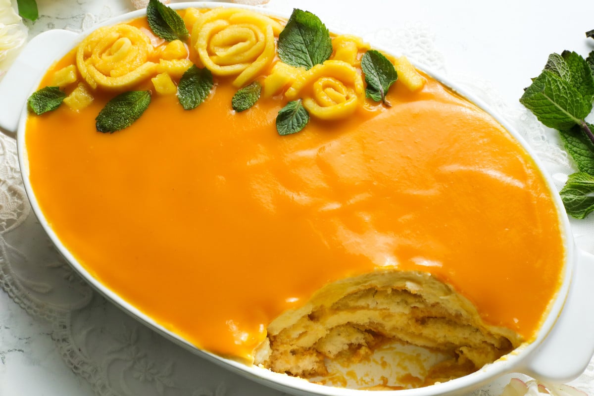 Mango Tira misu in a white oval dish topped with mangoes and mint leaves.