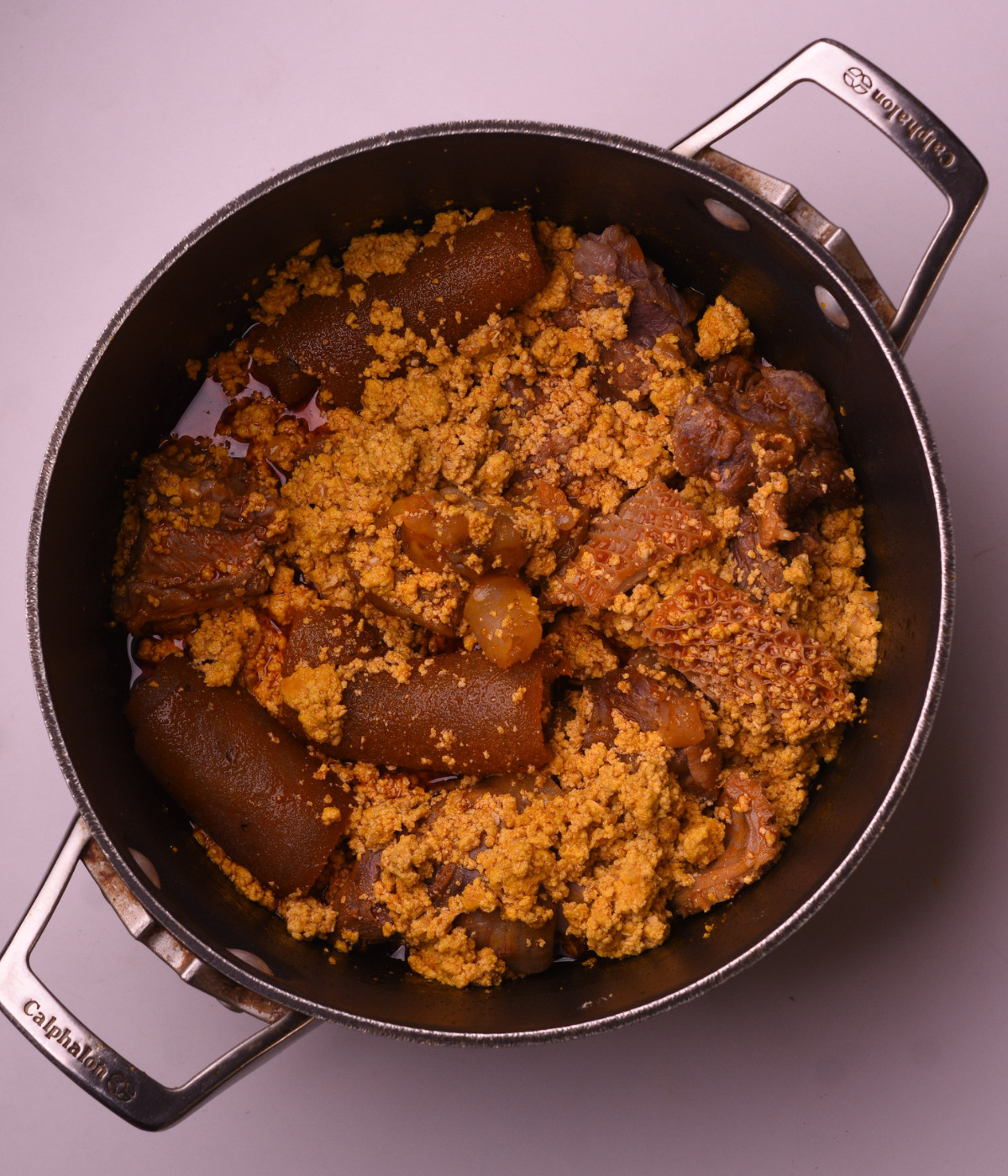 Palm oil cooking, assorted meat and egusi in a black pot.