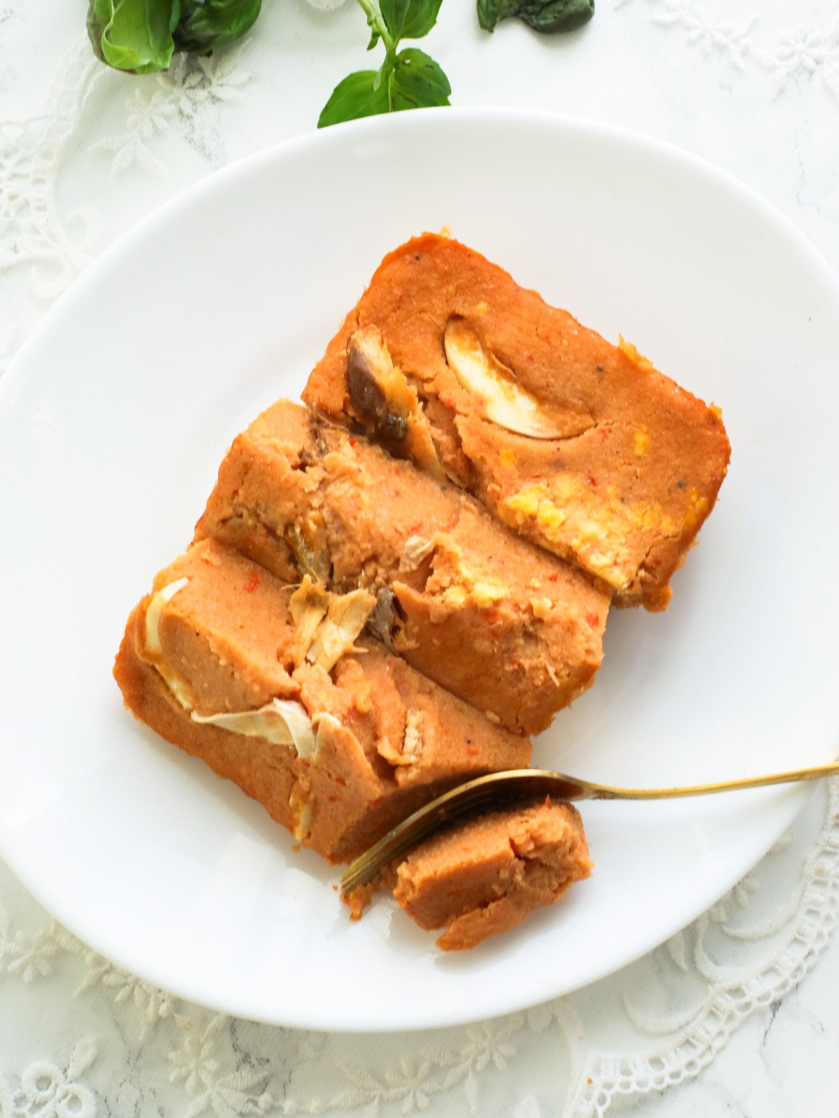 Three moi moi slices on a white plate with a gold fork.
