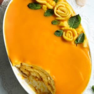 Tiramisu made with mangoes and pulp in an oval dish with mint leaves.