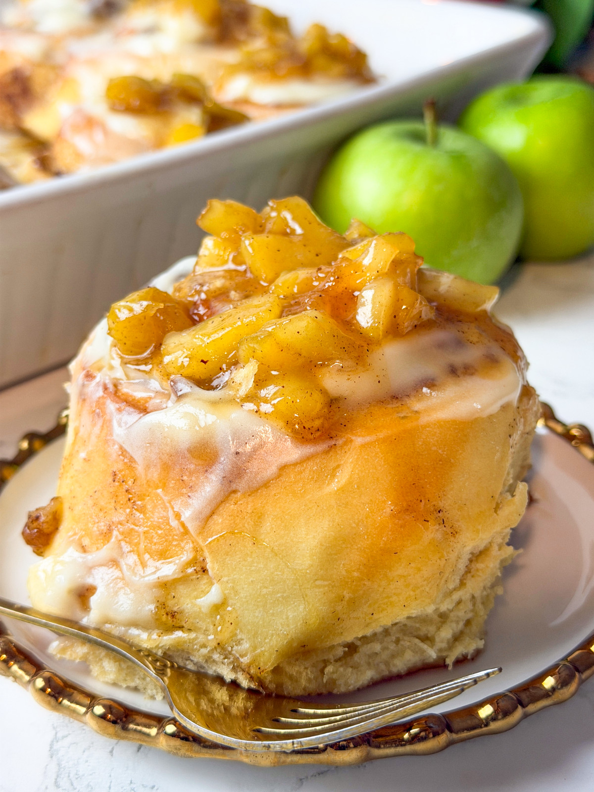 Apple cinnamon roll on a white and gold plate with a fork.