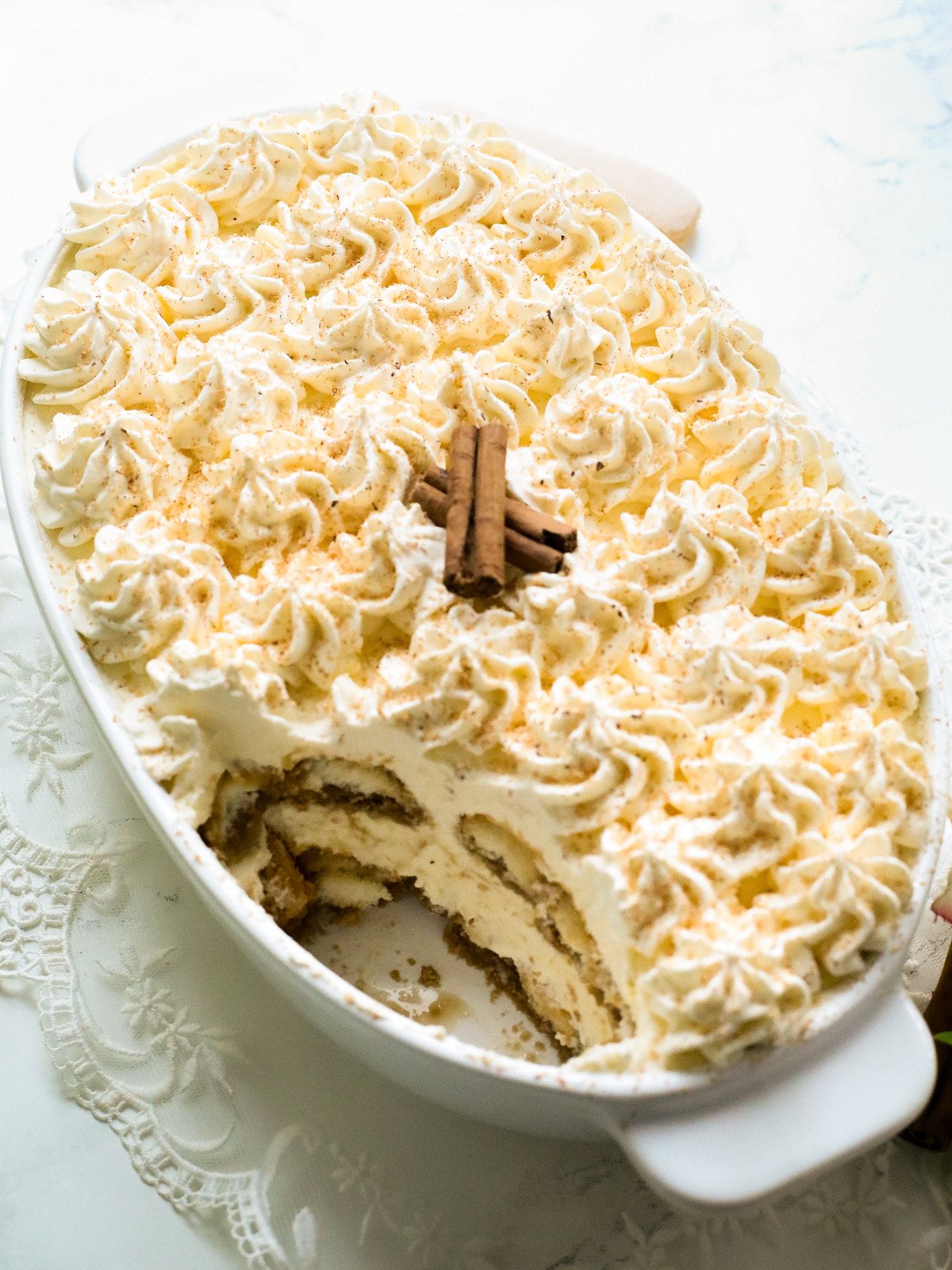 Egg nogg tiramisu in an oval dish with cinnamon sticks and nutmeg on top.