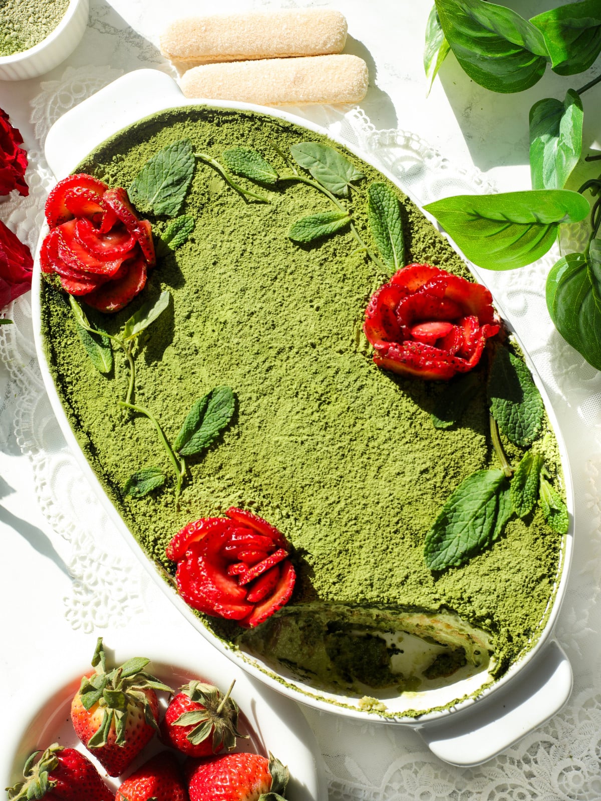 Matcha with strawberry tiramisu in a white oval dish. Roses and matcha powder on top.