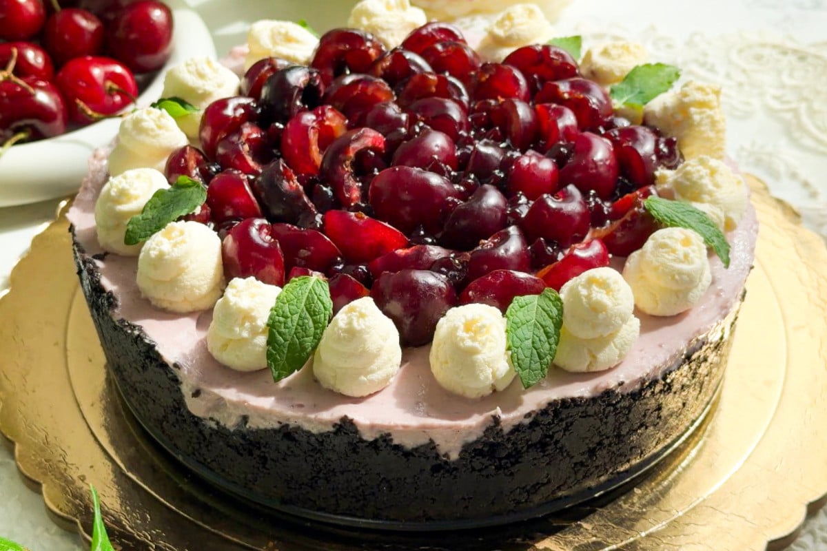 Cherry cheesecake on a gold board with whipped cream and mint leaves.