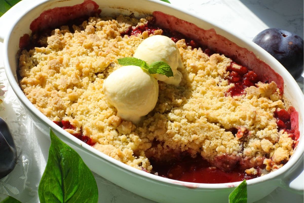 Plums crumble served with ice cream and a mint leaf.