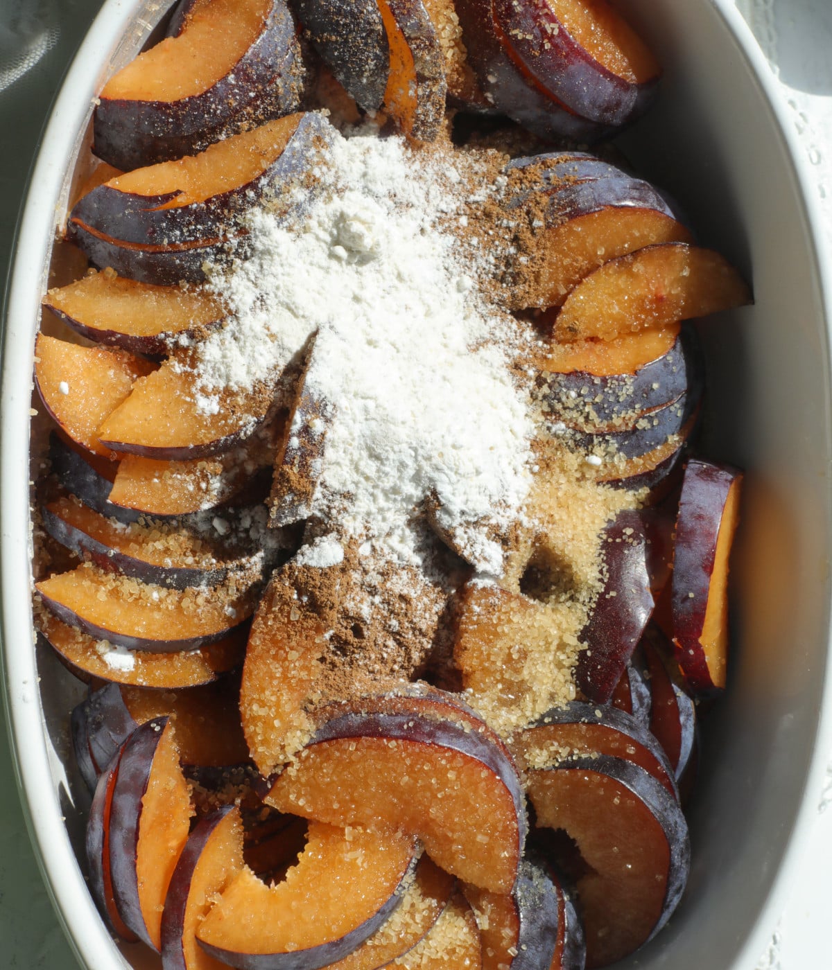 Sliced plums, sugar, flour and lemon in a dish.